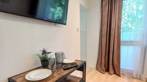 Un salon moderne avec un téléviseur à écran plat fixé au mur, une table à manger en bois avec une assiette blanche, une télécommande et une plante en pot.