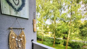 Un balcon agrémenté d’une décoration en forme de cœur, d’une suspension murale en macramé et de fleurs roses.