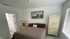 Un dormitorio con una cama grande, una mesita de noche con lámpara, un armario y un cuadro en la pared.