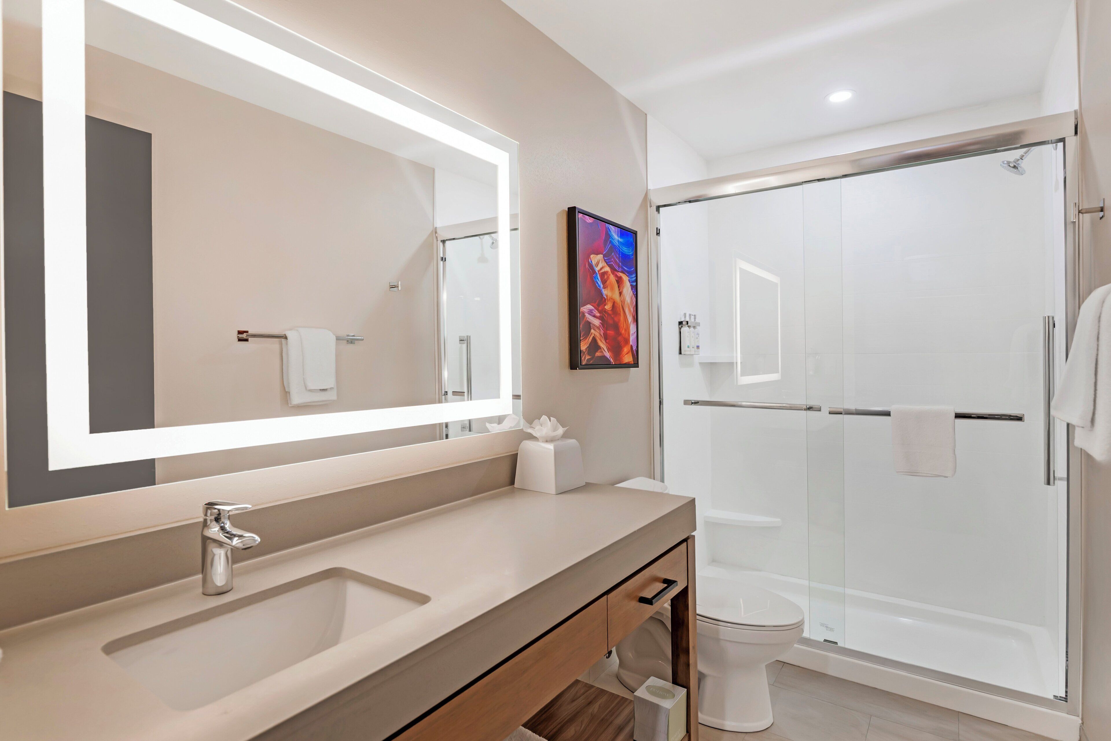 Un baño moderno con un espejo grande, un lavamanos, un inodoro y una ducha con mampara de cristal.