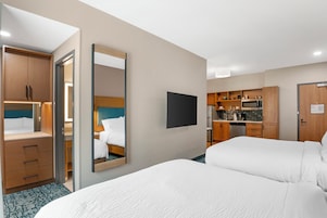 Habitación de hotel con cama, escritorio, espejo y kitchenette.