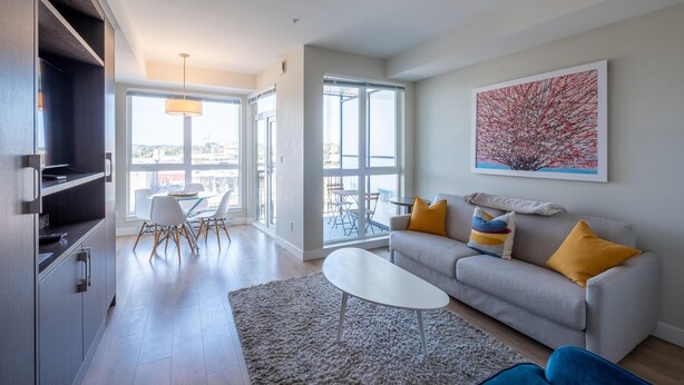 A modern living room with a sofa, coffee table, and dining area. - Chic Downtown Suite & People-Watching Deck (Victoria Central British Columbia Provincial Government)