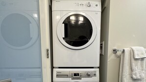 A compact, two-door laundry room with a front-loading washer and dryer. - Chic Downtown Suite & People-Watching Deck (Victoria Central British Columbia Provincial Government)