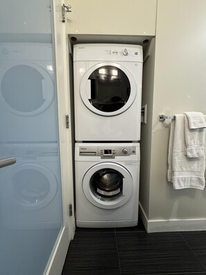 A compact, two-door laundry room with a front-loading washer and dryer. - Chic Downtown Suite & People-Watching Deck (Victoria Central British Columbia Provincial Government)