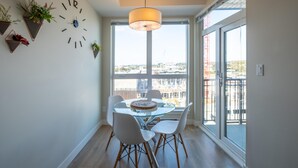 A dining area with a round glass table, white chairs, a clock, and potted plants on the wall. - Chic Downtown Suite & People-Watching Deck (Victoria Central British Columbia Provincial Government)