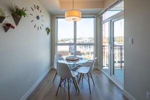 A dining area with a round glass table, white chairs, a clock, and potted plants on the wall. - Chic Downtown Suite & People-Watching Deck (Victoria Central British Columbia Provincial Government)