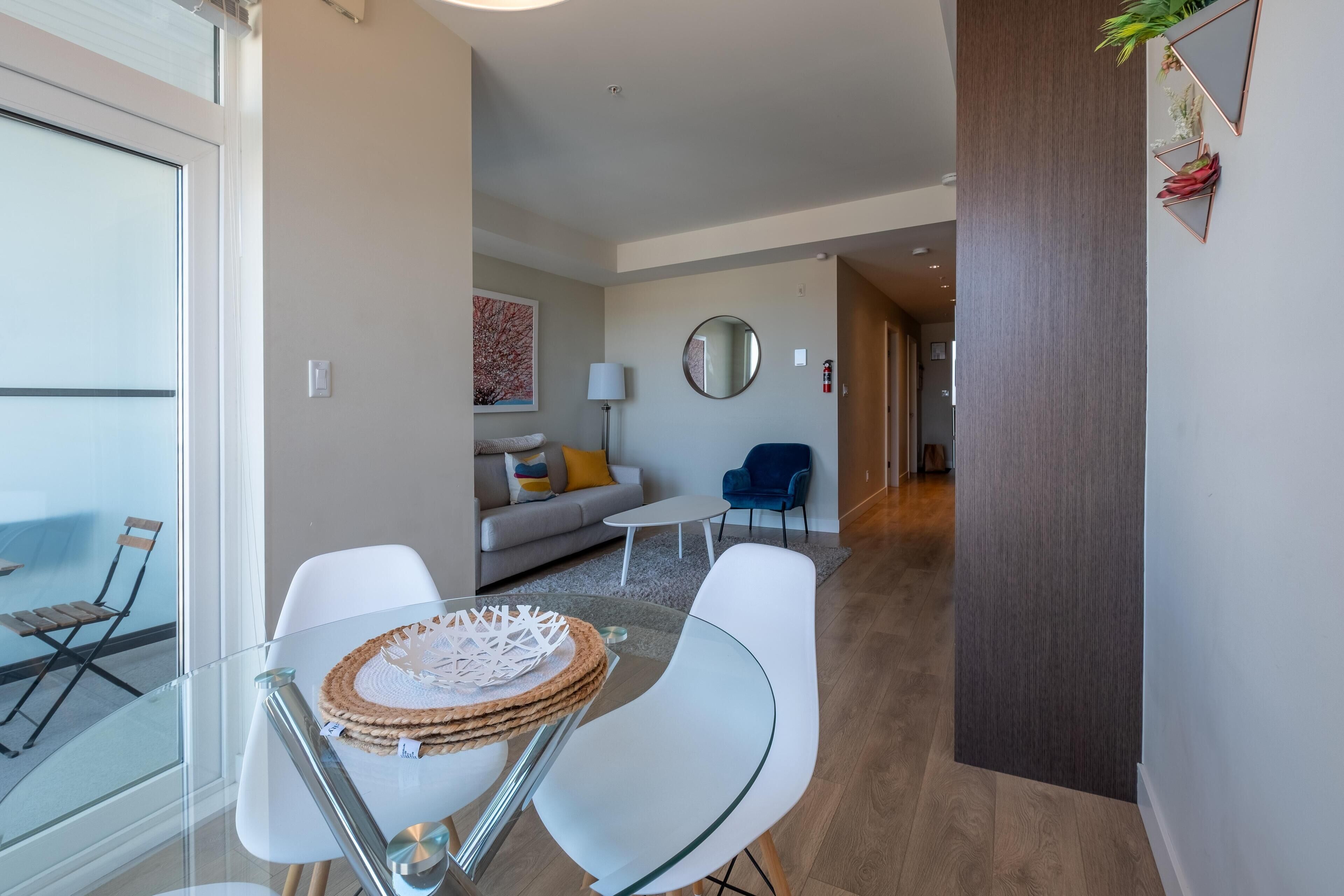 Un salon moderne avec une table en verre, des chaises blanches, un canapé et un fauteuil bleu.