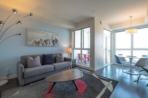 Ein modernes Wohnzimmer mit grauem Sofa, einem Couchtisch, einem Stadtbildgemälde und einem Essbereich mit Stühlen und Tisch.