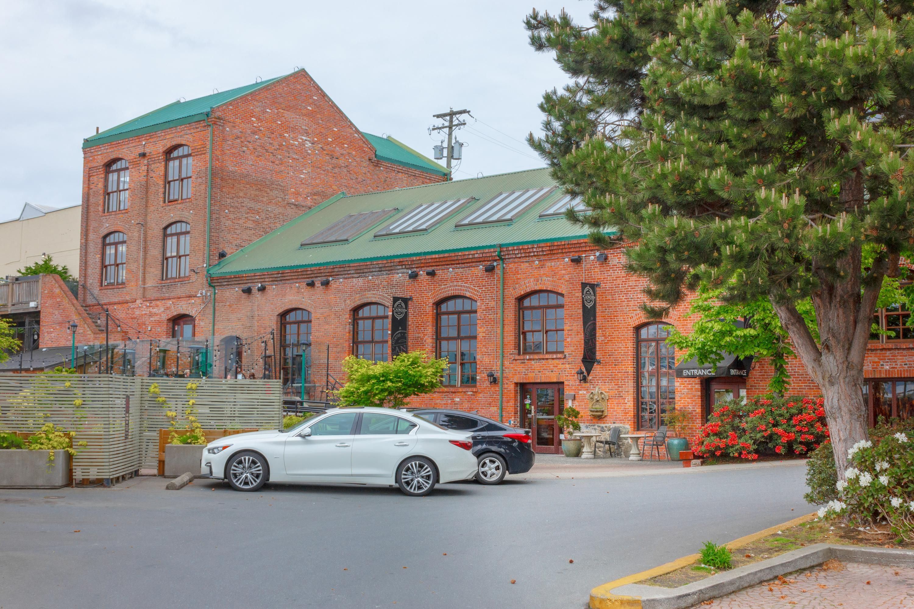A brick building with a green roof, a car parked in front, and a tree with red flowers.