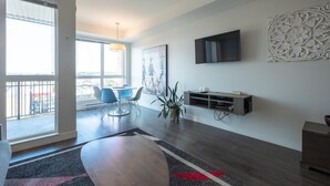 A modern living room with a dining area, large windows, a flat-screen TV, and a decorative wall piece. - Panoramic City Views and Modern Style Condo (Victoria Central British Columbia Provincial Government)