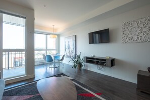 Ein modernes Wohnzimmer mit Essbereich, großen Fenstern, einem Flachbildfernseher und einem Wandkunstwerk.