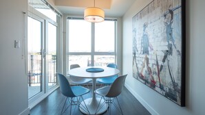 A modern dining area with a round table, four chairs, a pendant light, and a large abstract painting on the wall. - Panoramic City Views and Modern Style Condo (Victoria Central British Columbia Provincial Government)