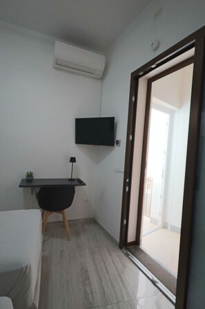 A modern room with a flat-screen TV mounted on the wall, a small desk with a lamp, and a sliding glass door leading to an outdoor area.