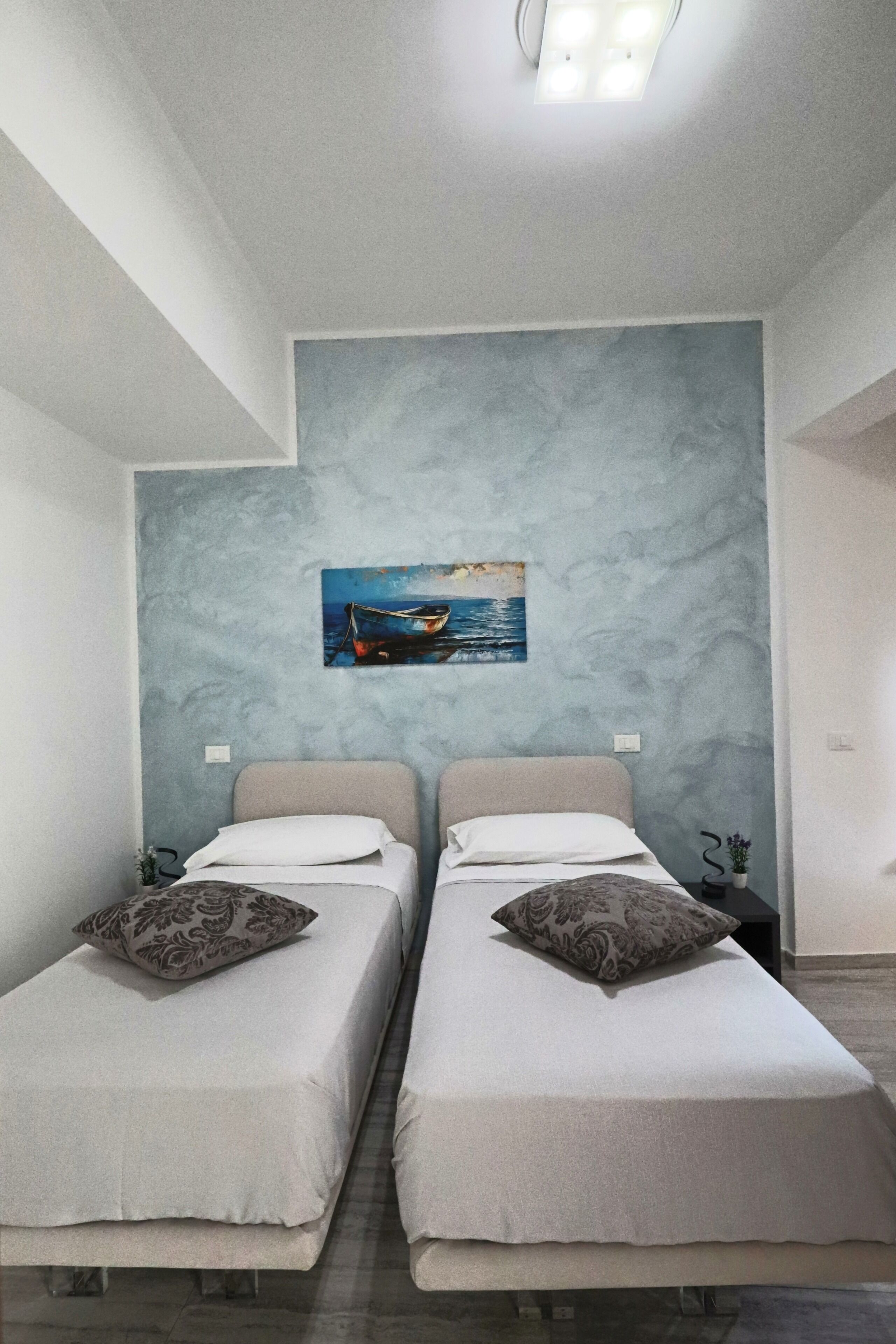 Ein Schlafzimmer mit zwei Betten, einem Bild eines Bootes an der Wand und einem Nachttisch mit einer Lampe.