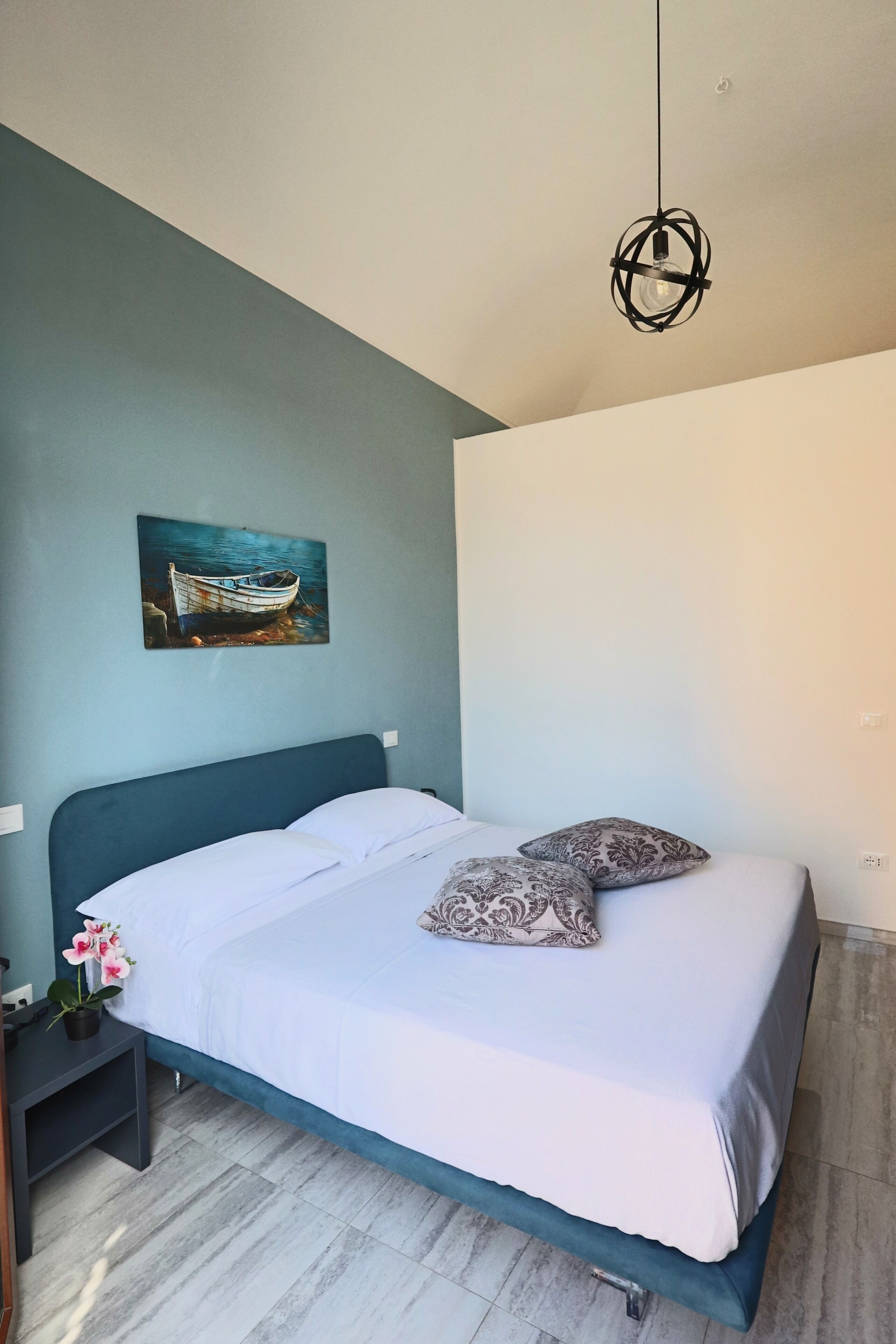 Una camera da letto con un letto, un comodino, una pianta in vaso e un quadro appeso al muro.