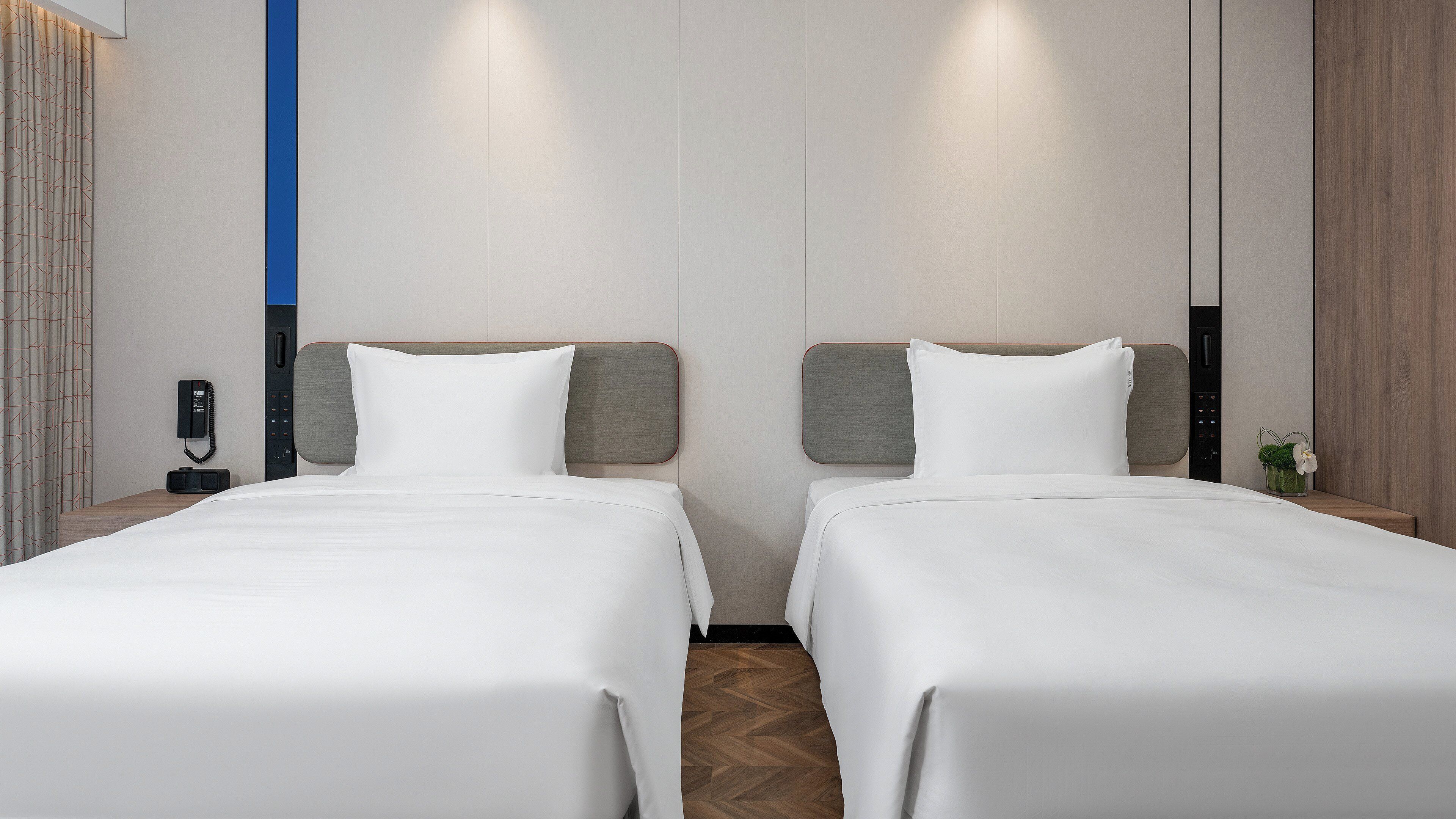 Ein Hotelzimmer mit zwei Betten, einem Nachttischtelefon und einer kleinen Pflanze auf dem Nachttisch.