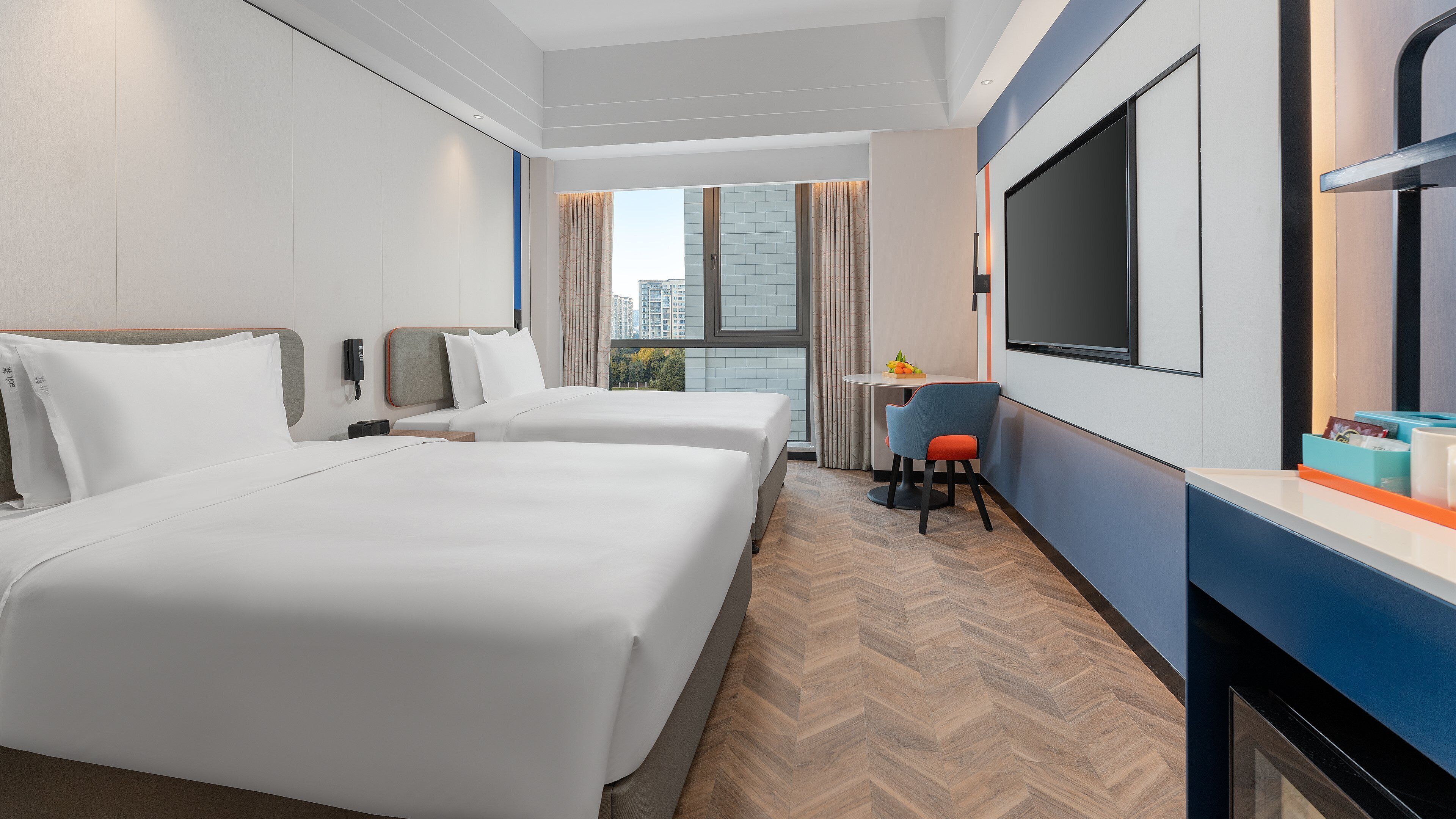 A hotel room with two beds, a desk with a chair, a TV, and a window with curtains.