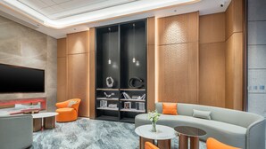 A modern living room with a flat-screen TV, orange armchairs, a grey sofa, and a bookshelf with decorative items. - Holiday Inn Express Chengdu Shuangliu Airport by IHG (Chengdu)