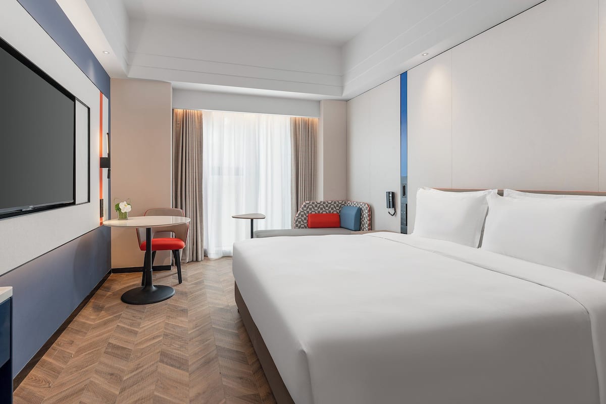 A modern hotel room with a large bed, a desk with a chair, a television, and a small table.