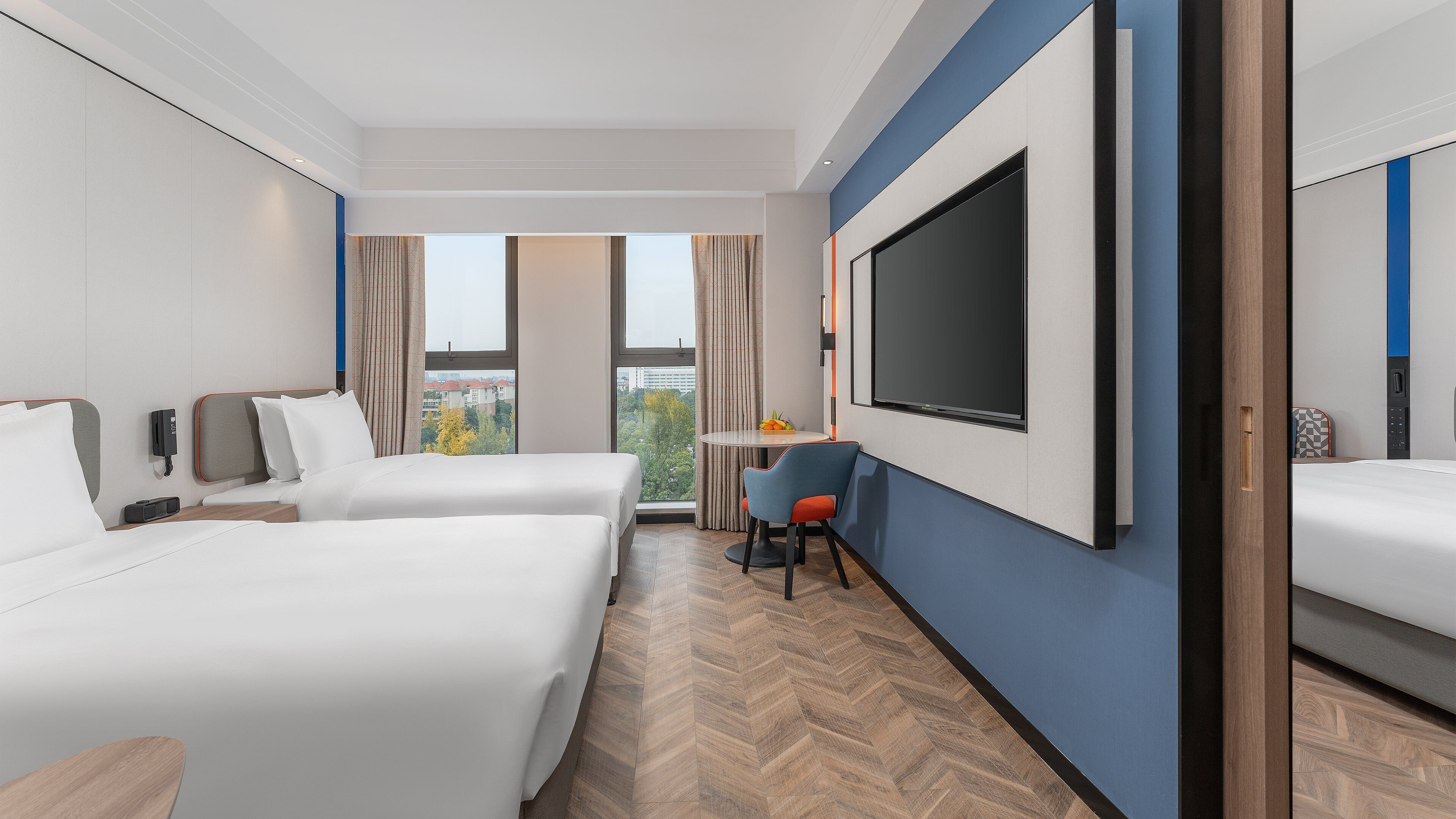 Une chambre d’hôtel avec deux lits, une télévision, un bureau avec une chaise et une fenêtre donnant sur un paysage agréable.