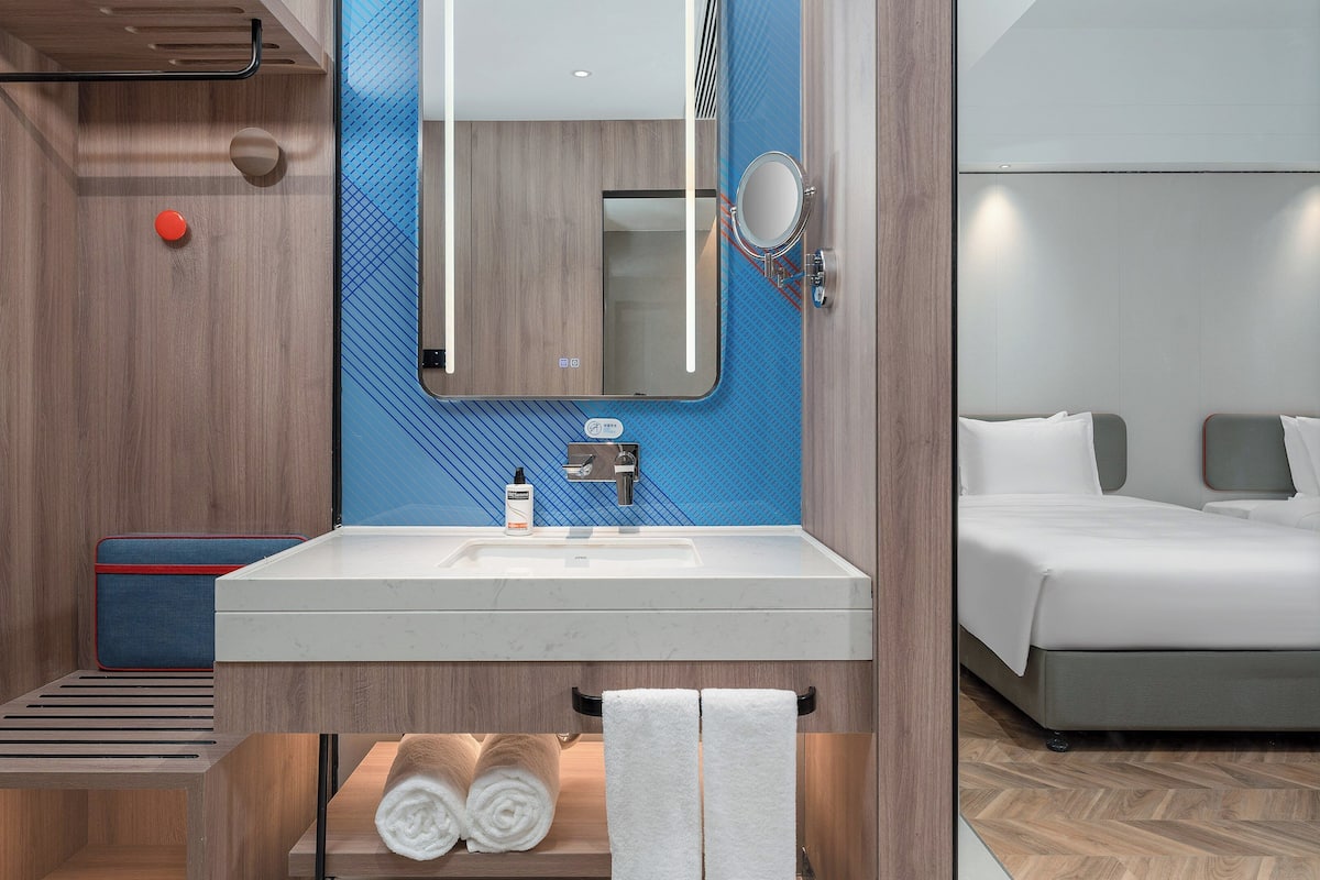 A modern bathroom with a wooden vanity, a large mirror, and a bed with white linens.