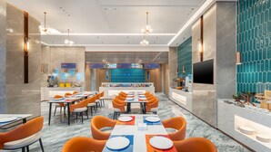 A modern hotel dining area with multiple tables, orange chairs, and a TV screen. - Holiday Inn Express Chengdu Shuangliu Airport by IHG (Chengdu)
