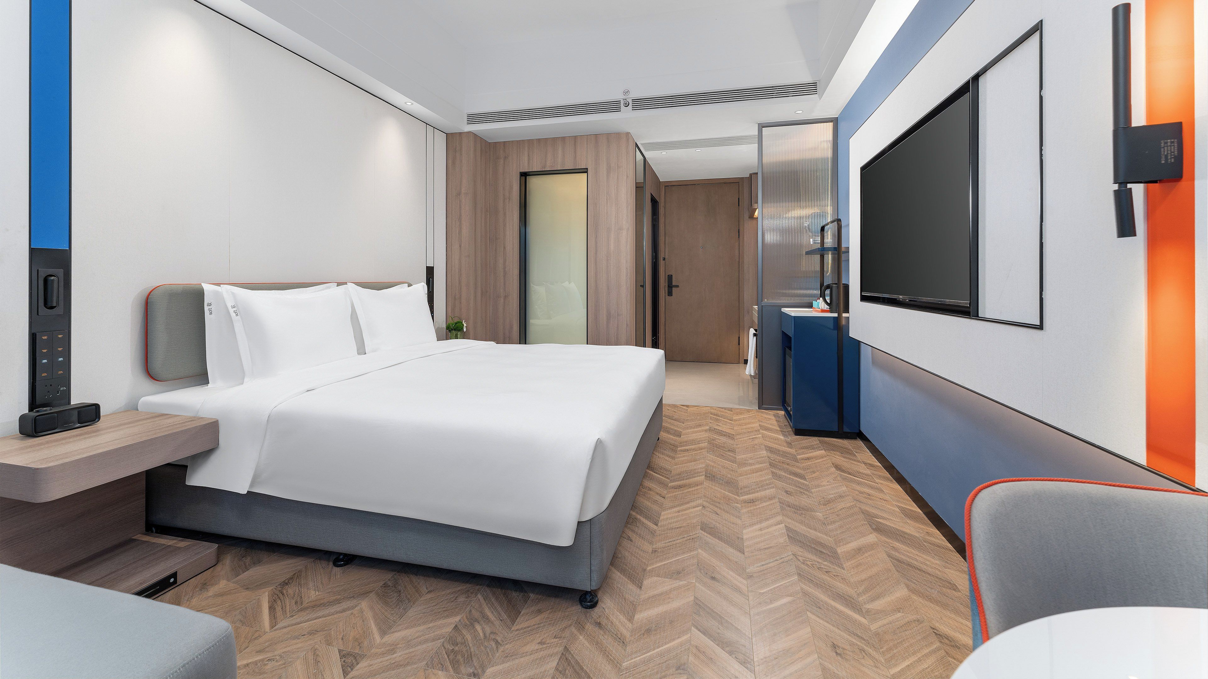A modern hotel room with a bed, a desk, a TV, and a minibar.