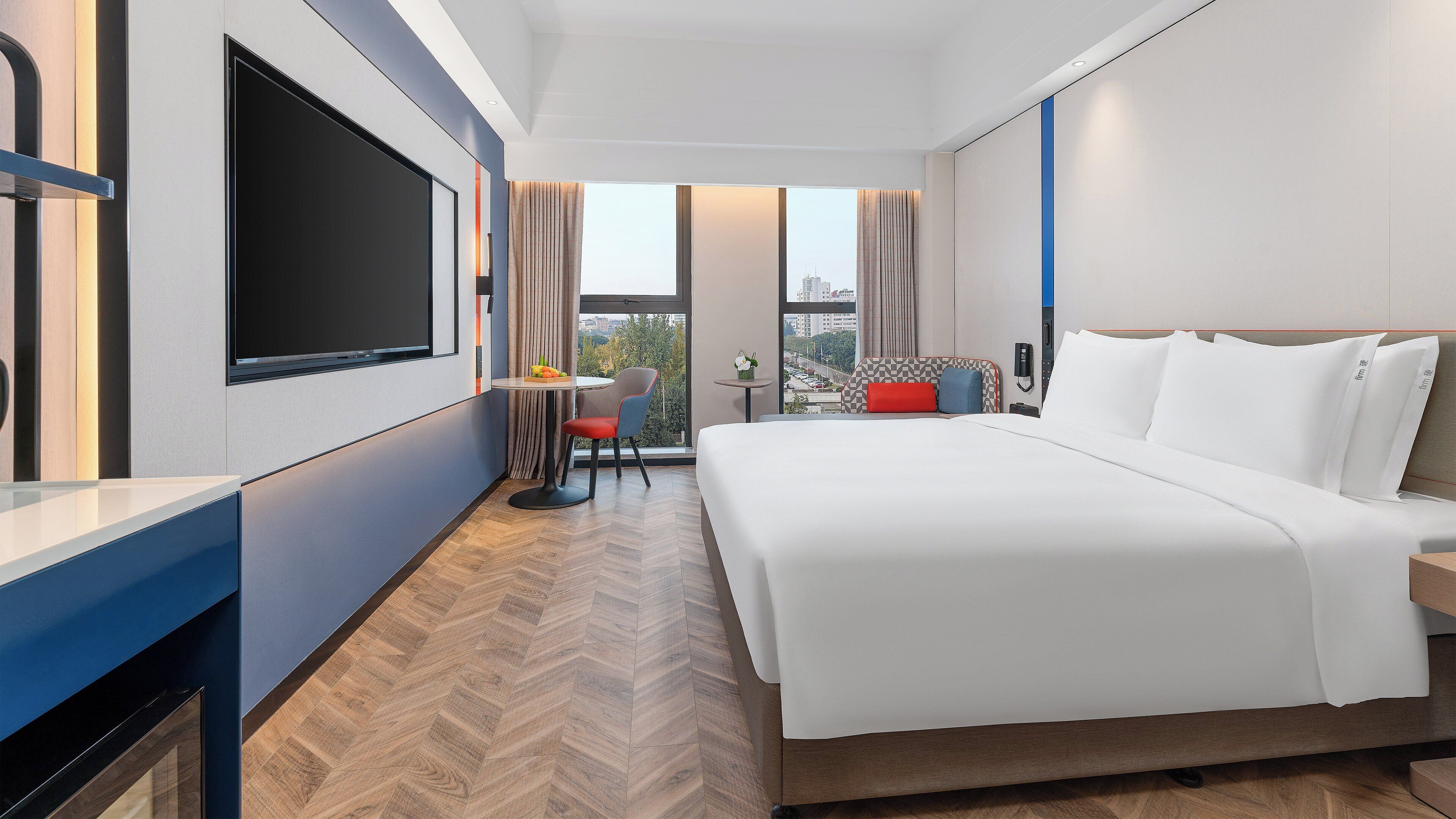 A hotel room with a large bed, a desk, a chair, a small table, and a TV.