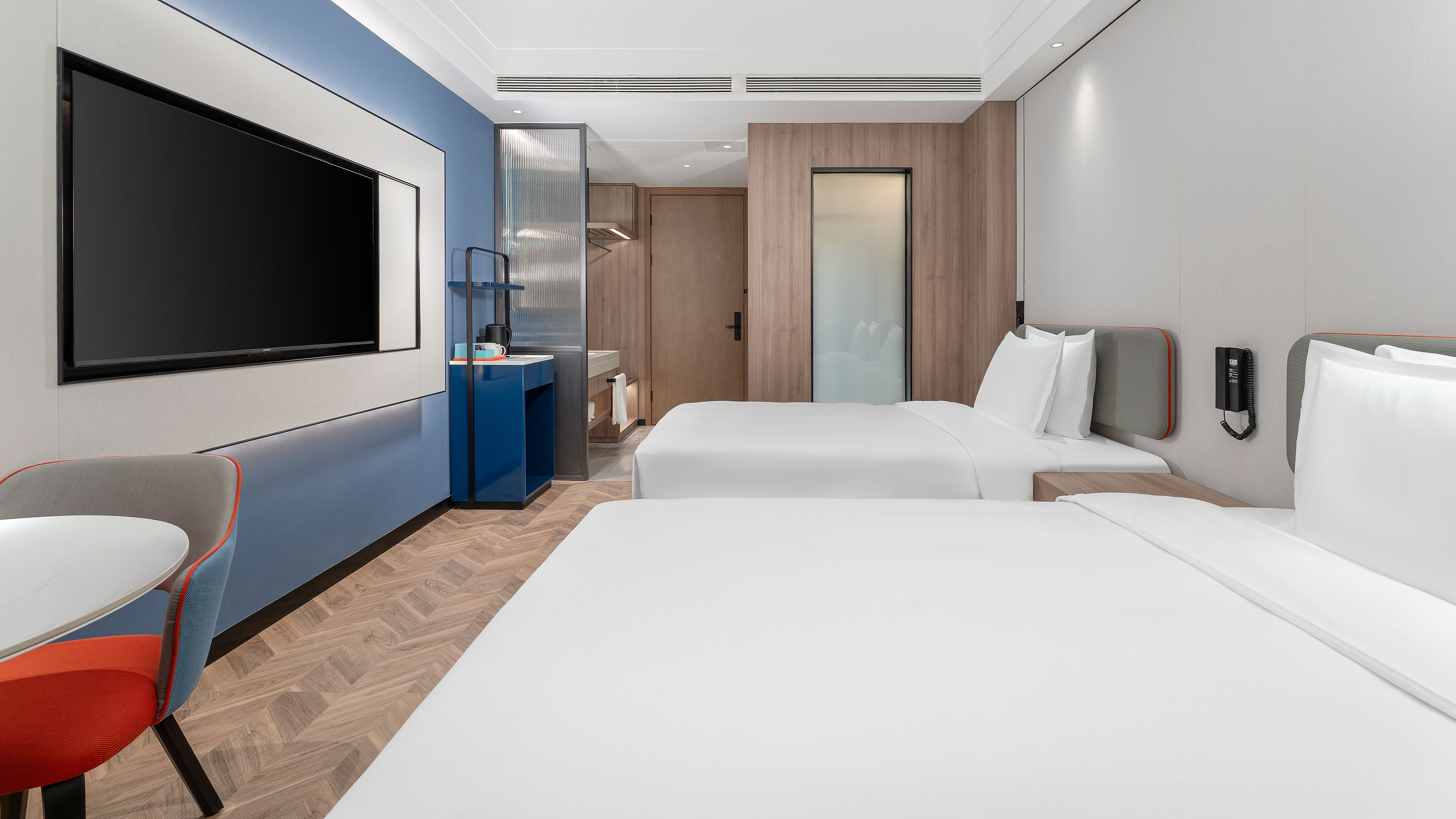 Une chambre d’hôtel moderne équipée de deux lits, d’une télévision, d’un bureau et d’une chaise.