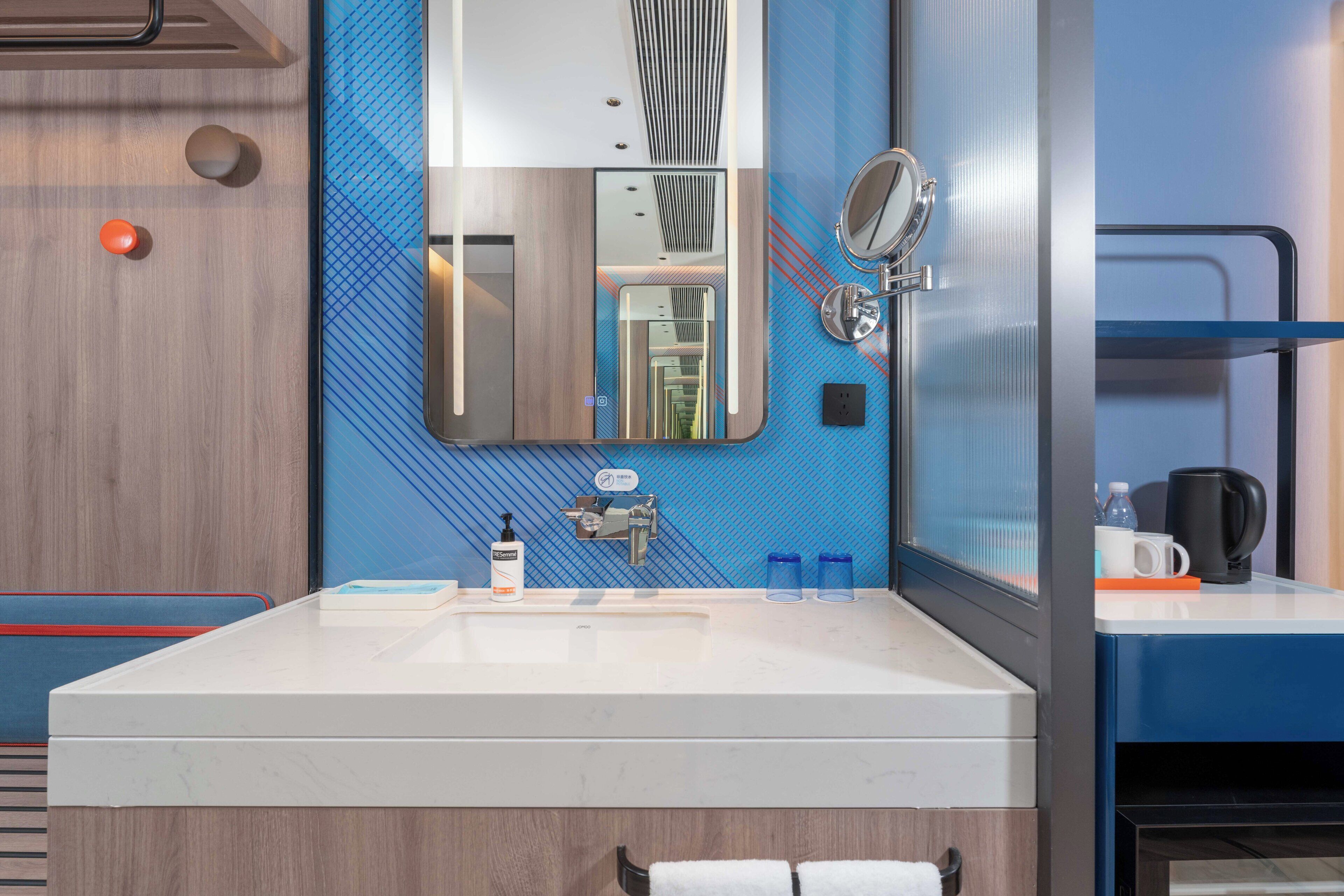 A modern bathroom with a large mirror, two sinks, and a blue patterned wall.