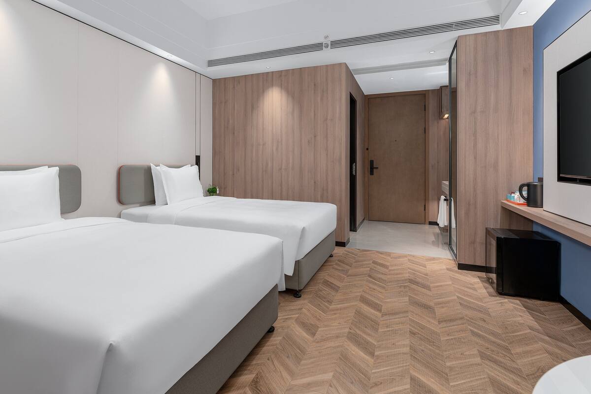 A modern hotel room with two beds, a TV, a small desk, and a bathroom.