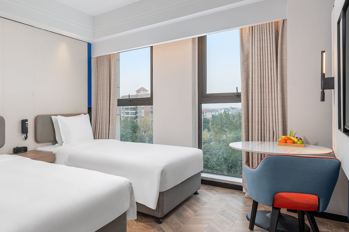 A hotel room with two beds, a small table with fruit, and a TV.