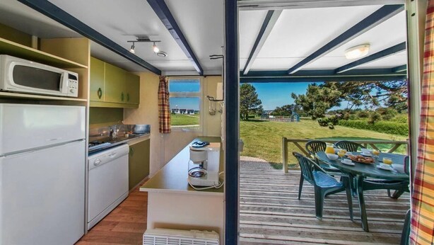 A compact kitchen with a microwave, stove, and coffee maker, leading to an outdoor dining area with a table and chairs. - ZEcamping 2 étoiles piscine couverte chiens acceptés hammam et jacuzzi (Plestin-les-Grèves)