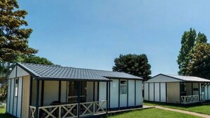 Two mobile homes with a porch and a small deck, set in a grassy area with trees in the background. - ZEcamping 2 étoiles piscine couverte chiens acceptés hammam et jacuzzi (Plestin-les-Grèves)