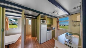 A compact kitchen with a microwave, refrigerator, and stove. There is a bench and a window with a view of a green landscape. - ZEcamping 2 étoiles piscine couverte chiens acceptés hammam et jacuzzi (Plestin-les-Grèves)