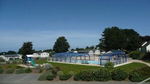 A pool area with a covered deck, surrounded by greenery and residential buildings. - ZEcamping 2 étoiles piscine couverte chiens acceptés hammam et jacuzzi (Plestin-les-Grèves)