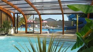 An indoor swimming pool with a covered area, lounge chairs, and a water slide. - ZEcamping 4 étoiles animé parc aquatique locatif TV 30m2 4 pers (Fouesnant)