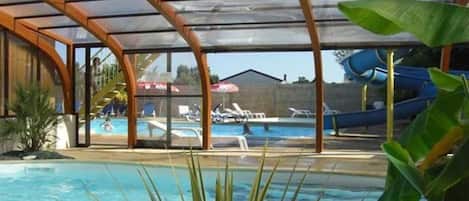 An indoor swimming pool with a covered area, lounge chairs, and a water slide.