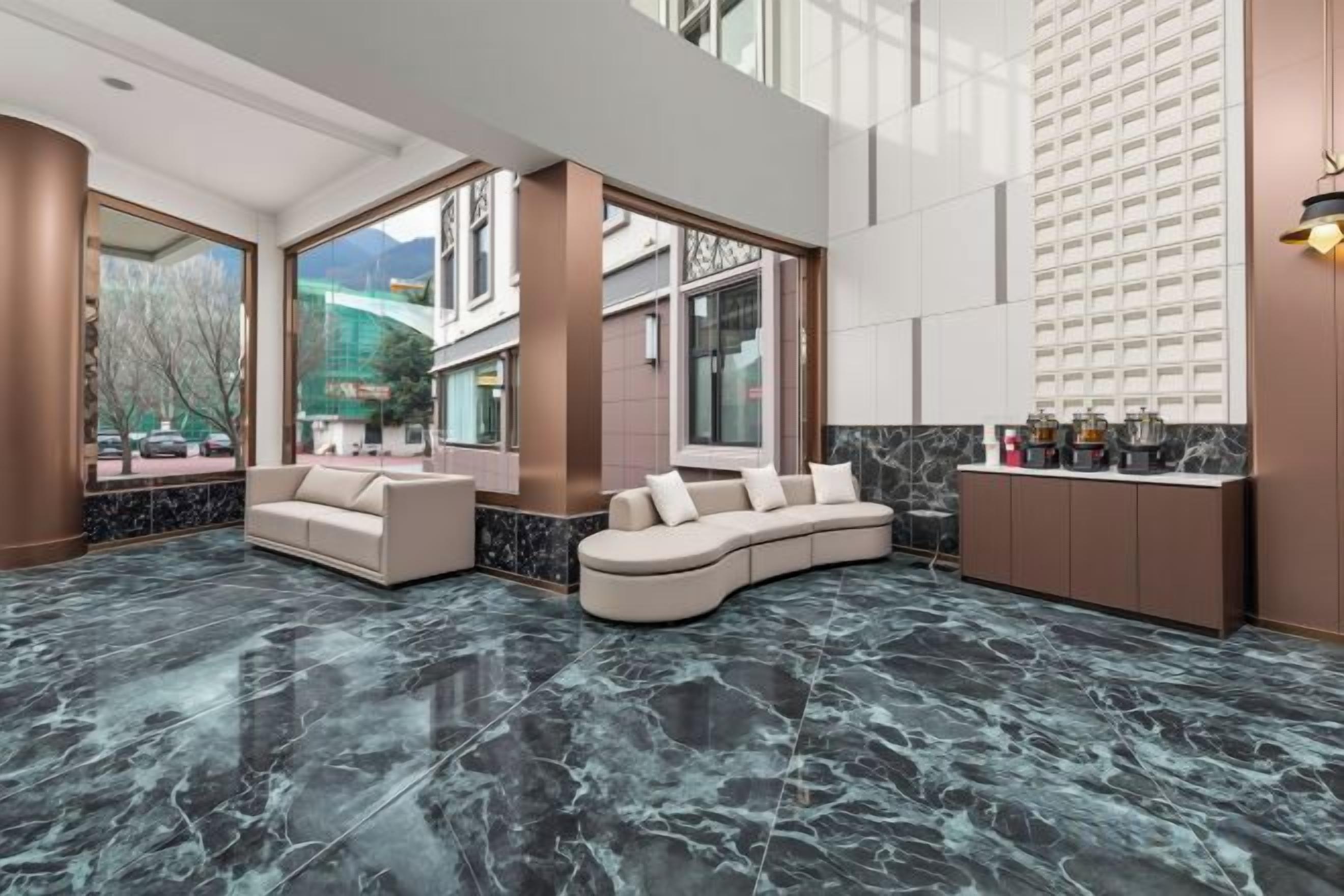 A modern hotel lobby with a curved sofa, a bar area, and large windows offering a view of the city.