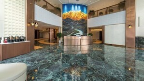 Eine Hotelhalle mit Marmorboden, einer Rezeption und einem Wandbild einer Berglandschaft.