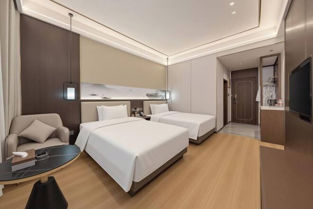 Une chambre d’hôtel avec deux lits, un canapé, une petite table, une télévision et une salle de bain visible à travers une porte ouverte.