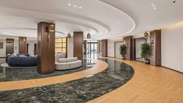 A spacious lobby with a curved marble floor, a seating area with sofas, and a reception desk.