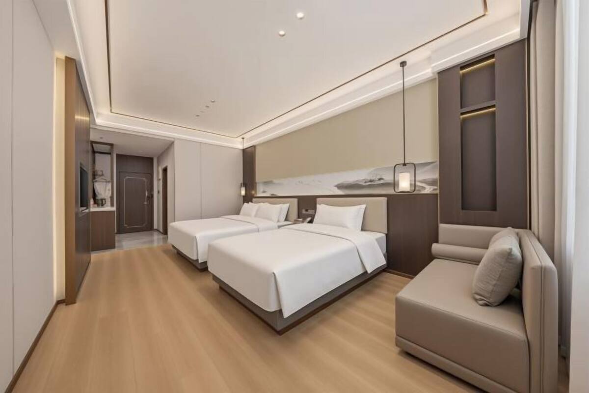 Une chambre d’hôtel moderne avec deux lits, un canapé, un grand miroir et un plancher en bois.