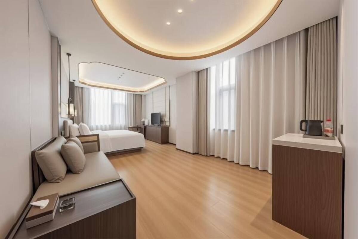 Une chambre d’hôtel moderne équipée d’un lit, d’un coin salon, d’un bureau et d’une grande fenêtre avec des rideaux.