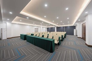 Un salón de conferencias con filas de sillas, piso alfombrado e iluminación empotrada en el techo.