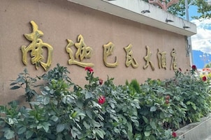 Un edificio con letras doradas de gran tamaño en la fachada, rodeado de follaje verde y flores rojas.