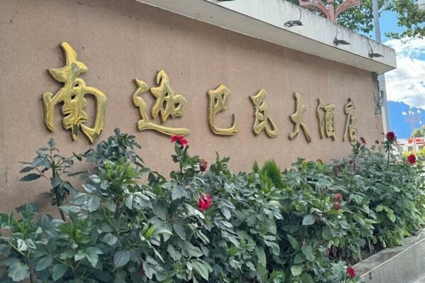 Un edificio con letras doradas de gran tamaño en la fachada, rodeado de follaje verde y flores rojas.