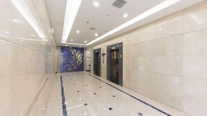 A modern hotel corridor with a polished marble floor, a decorative wall mural, and a pair of elevators. - Huali Hotel (Kunshan Golden Eagle International Shopping Center) (Kunshan)
