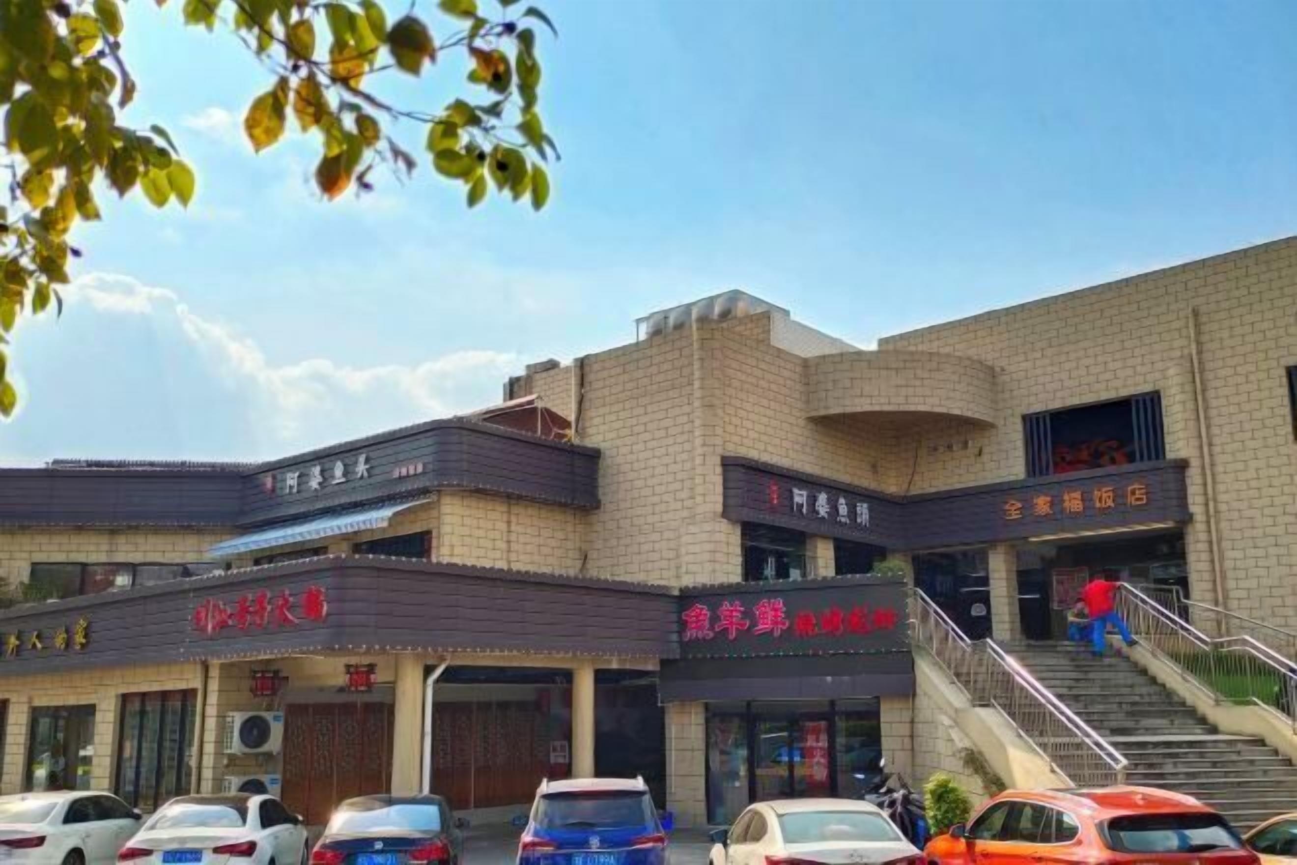 Un edificio con varias fachadas comerciales, incluyendo un restaurante y una tienda de abarrotes. Hay coches estacionados al frente, y una persona bajando por unas escaleras.