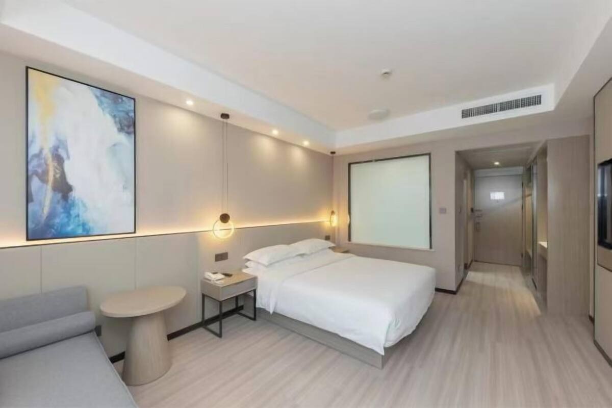 Una habitación de hotel moderna con una cama grande, una mesita de noche, una pequeña mesa redonda y un cuadro abstracto de gran tamaño en la pared.